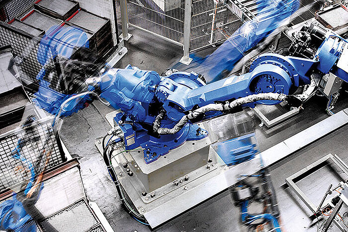 Großer blauer Industrieroboter mit beweglichem Greifarm in einer Fabrikhalle, Bewegungsunschärfe zeigt schnelle Bewegung