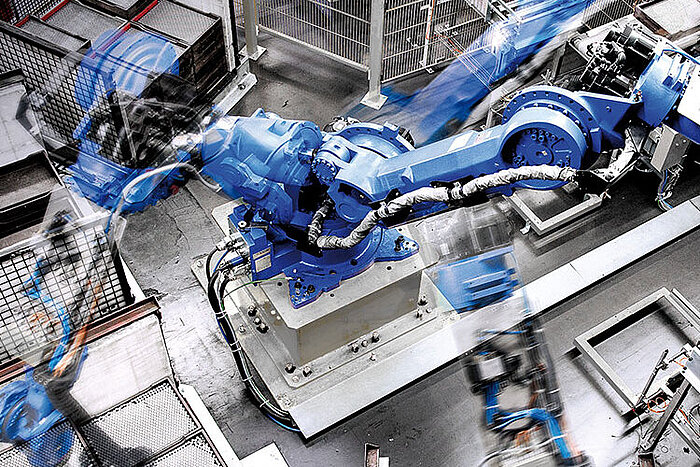 Großer blauer Industrieroboter mit beweglichem Greifarm in einer Fabrikhalle, Bewegungsunschärfe zeigt schnelle Bewegung