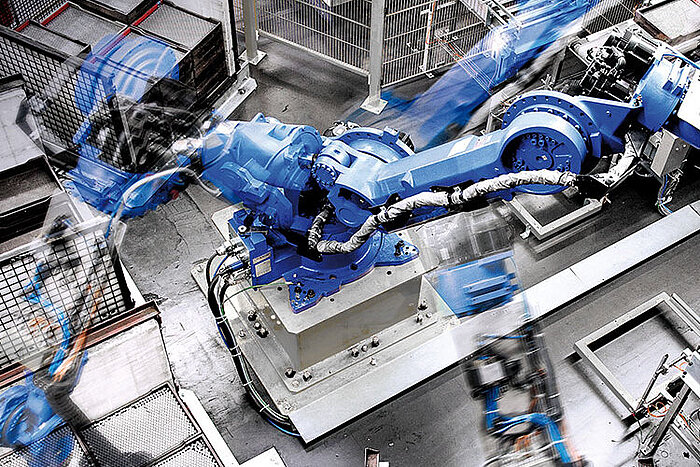 Braço robótico industrial azul em movimento numa fábrica, captado com efeito de exposição longa entre grades metálicas