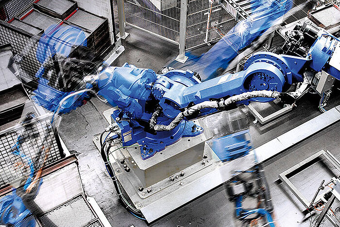 Brazo robótico industrial azul en movimiento dentro de una instalación de fabricación con vallas de seguridad metálicas