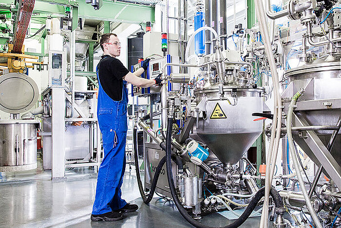 Techniker in blauer Latzhose bedient Steuergerät an industrieller Anlage mit Edelstahltanks und Rohrleitungen