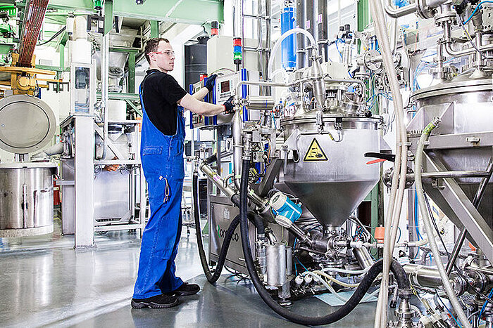 Técnico de macacão azul opera painel de controlo entre equipamentos industriais de aço inoxidável com tubagens